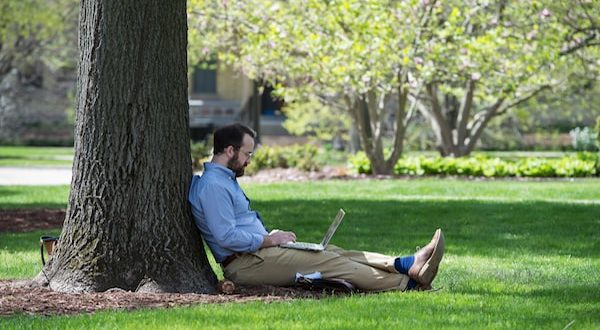 student leaning against tree in quad