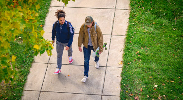 aerial view of two students walking on a paved path through a green grassy courtyard