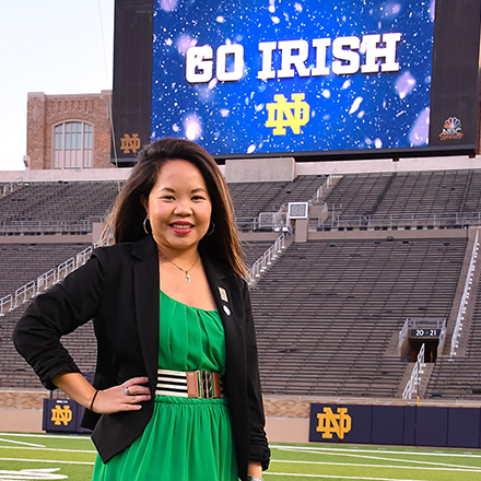 female student posing in the stadium. The sign behind her reads "Go Irish".