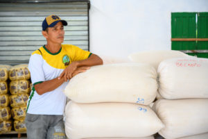A man leans on stacked white bags and wears a Notre Dame baseball cap