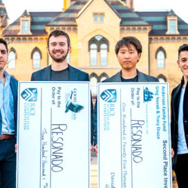 founders of resonado stand in front of the main building holding large cardboard checks from the rice competition