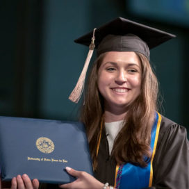 a woman graduate receives her diploma and smiles