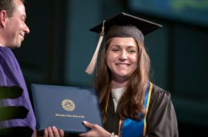 a woman graduate receives her diploma and smiles