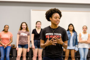 a woman stands in front of young women talking