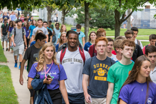a group of undergraduate students in Notre Dame gear walking outside on a sunny day