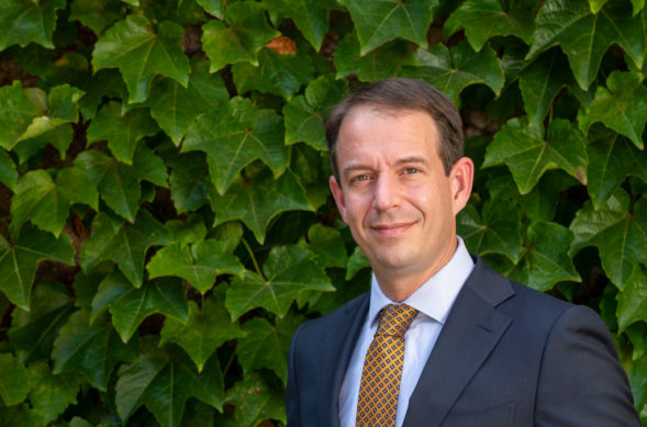 headshot of a man in business attire in front of a leafy green background