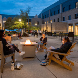 students sit around a firepit outside Mendoza College of Business