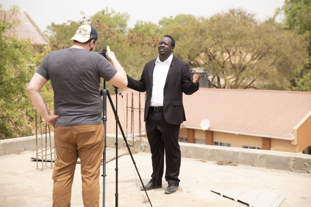 man speaking to camera while another films