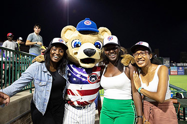 women posing with mascot at a baseball game