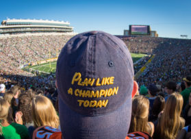 student wearing a play like a champion today hat at a packed football game