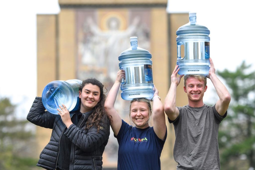 three students with water jugs on their heads on campus