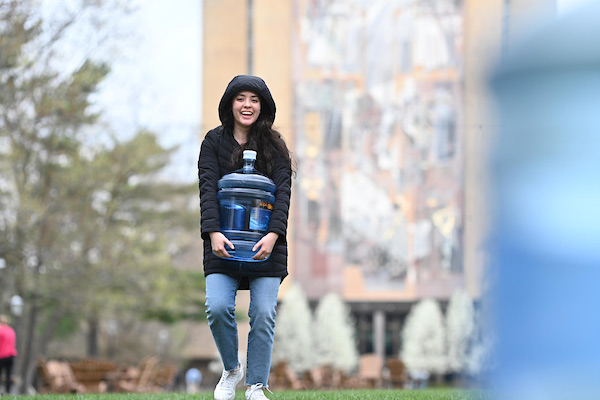 student carrying a water jug on the library green