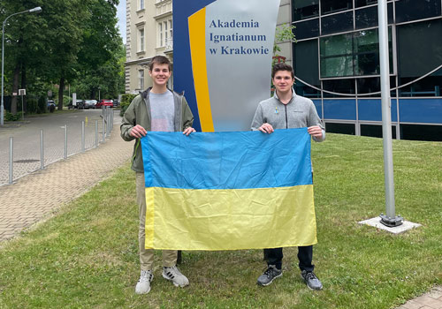 two students stand holding Ukrainian flag in front of university sign