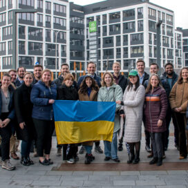 a group of students and advisors for the Meyer Frontlines program stand in front of buildings in Poland holding a Ukrainian flag.
