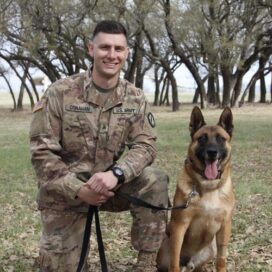 man in military uniform kneeling next to service dog