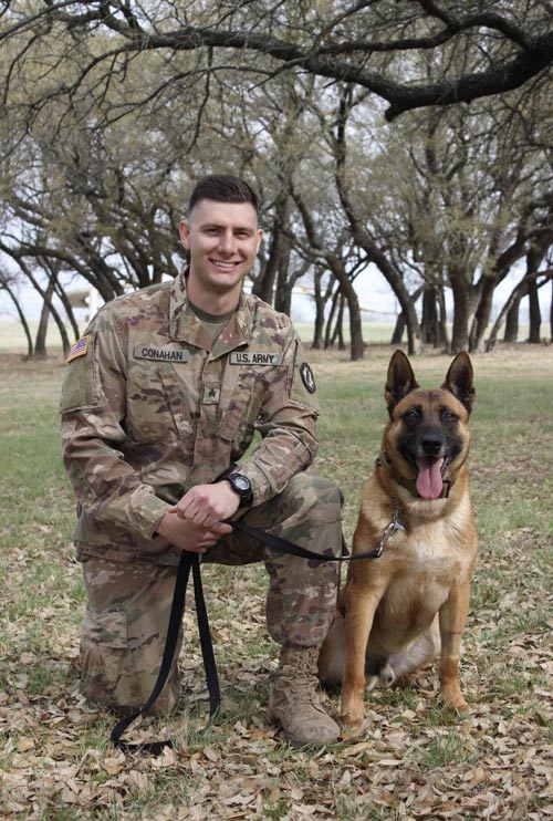 man in military uniform kneeling next to service dog