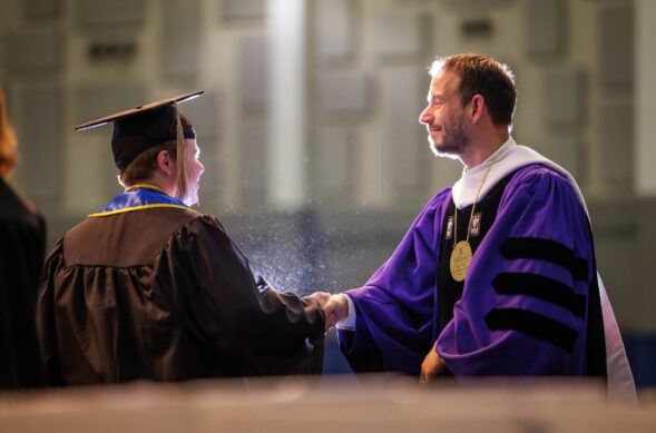 Dean in academic regalia shaking hands with a student in commencement attire