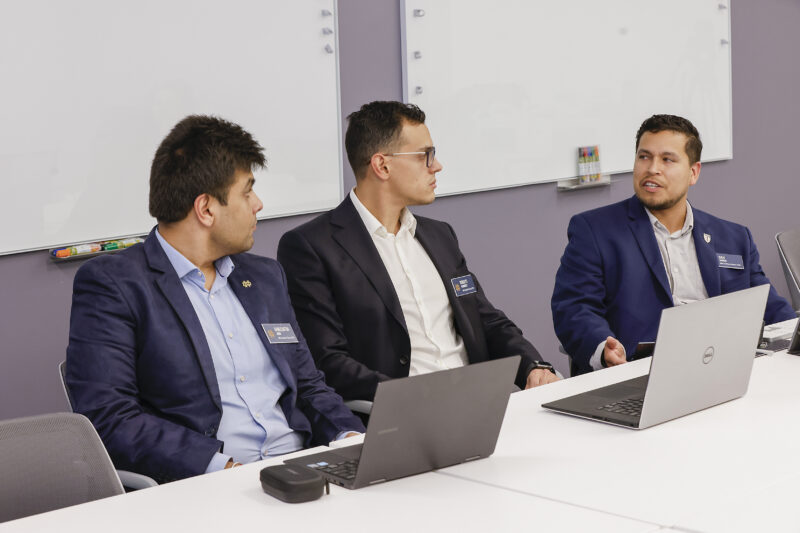 group of three wearing business professional discussing with laptops open