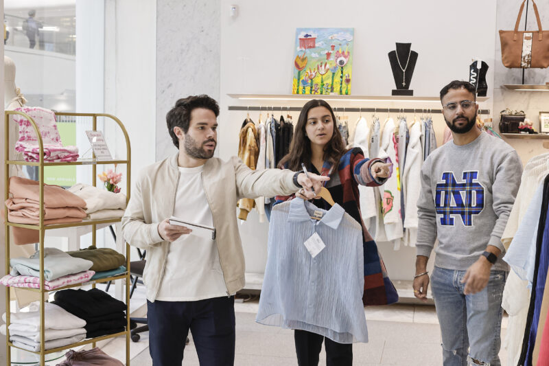 group of three pointing at a clothing rack inside a store