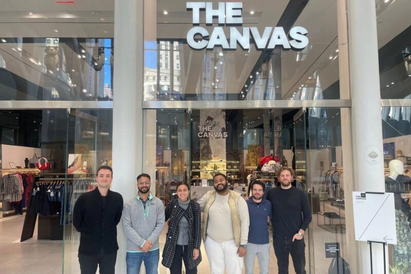 group of standing standing in front of a large glass storefront which reads "the Canvas"