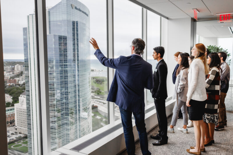 group dressed in business professional looking out a large glass wall onto a cityscape