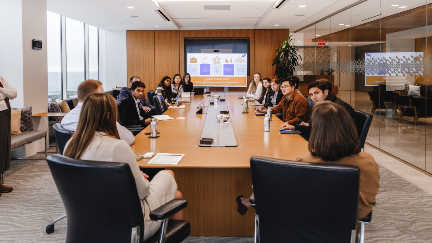 a dozen people seated around a large wooden desk