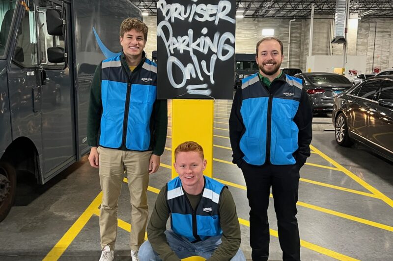 three young men wearing bright blue vests in a parking garage