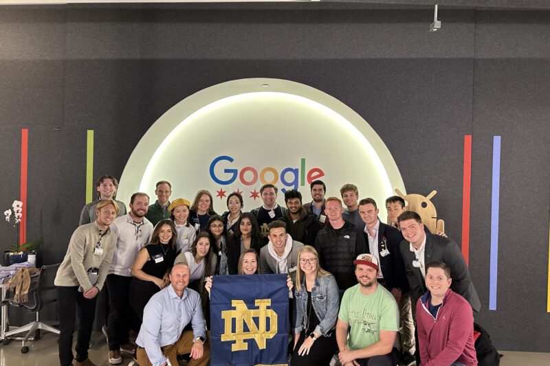 large group posing in front of a sign which reads "Google". A woman kneeling in front holds a large blue and gold ND Irish flag