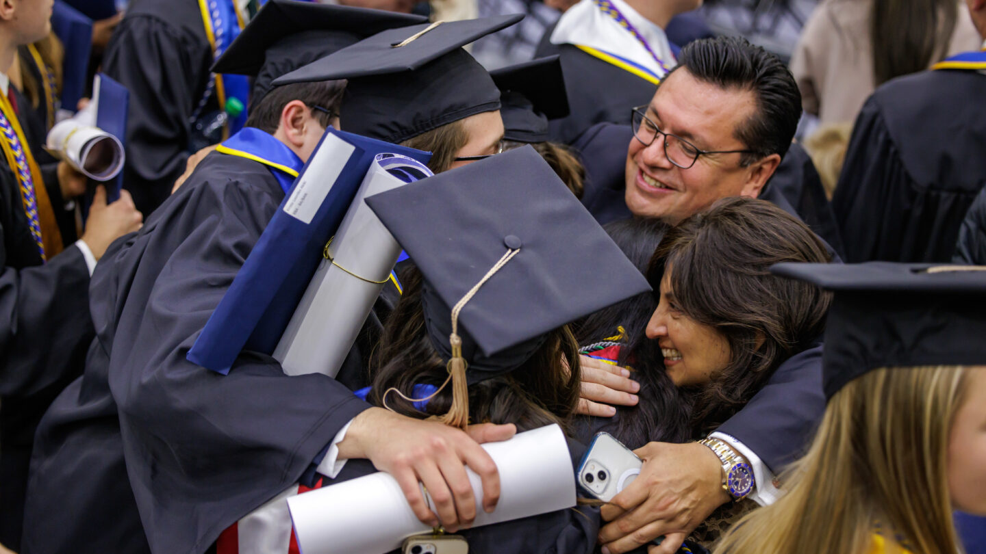 A group of people dressed in academic regalia and hug in celebration