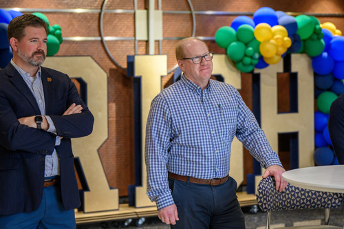 two men stand in the mendoza college of business atrium with an irish sign and ballons behind them.