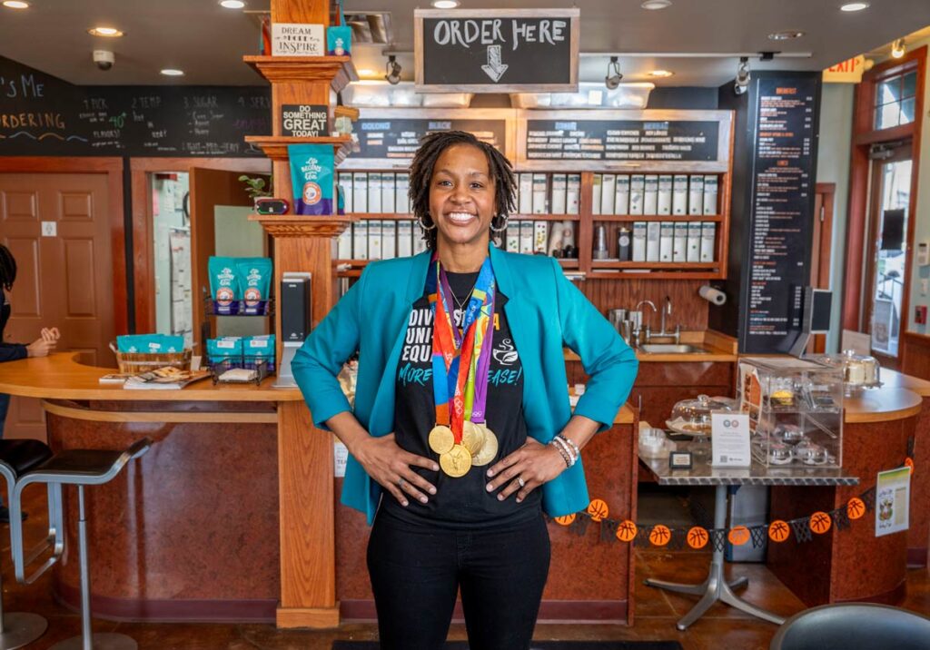 Tamika Catchings in front of the counter in her tea shop, wearing her gold medals