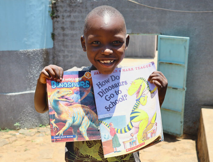 child holds up children's books and smiles into the camera