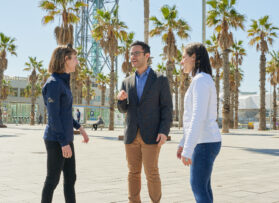 A discussion among three people set against a backdrop of vibrant palm trees, evoking a relaxed atmosphere.