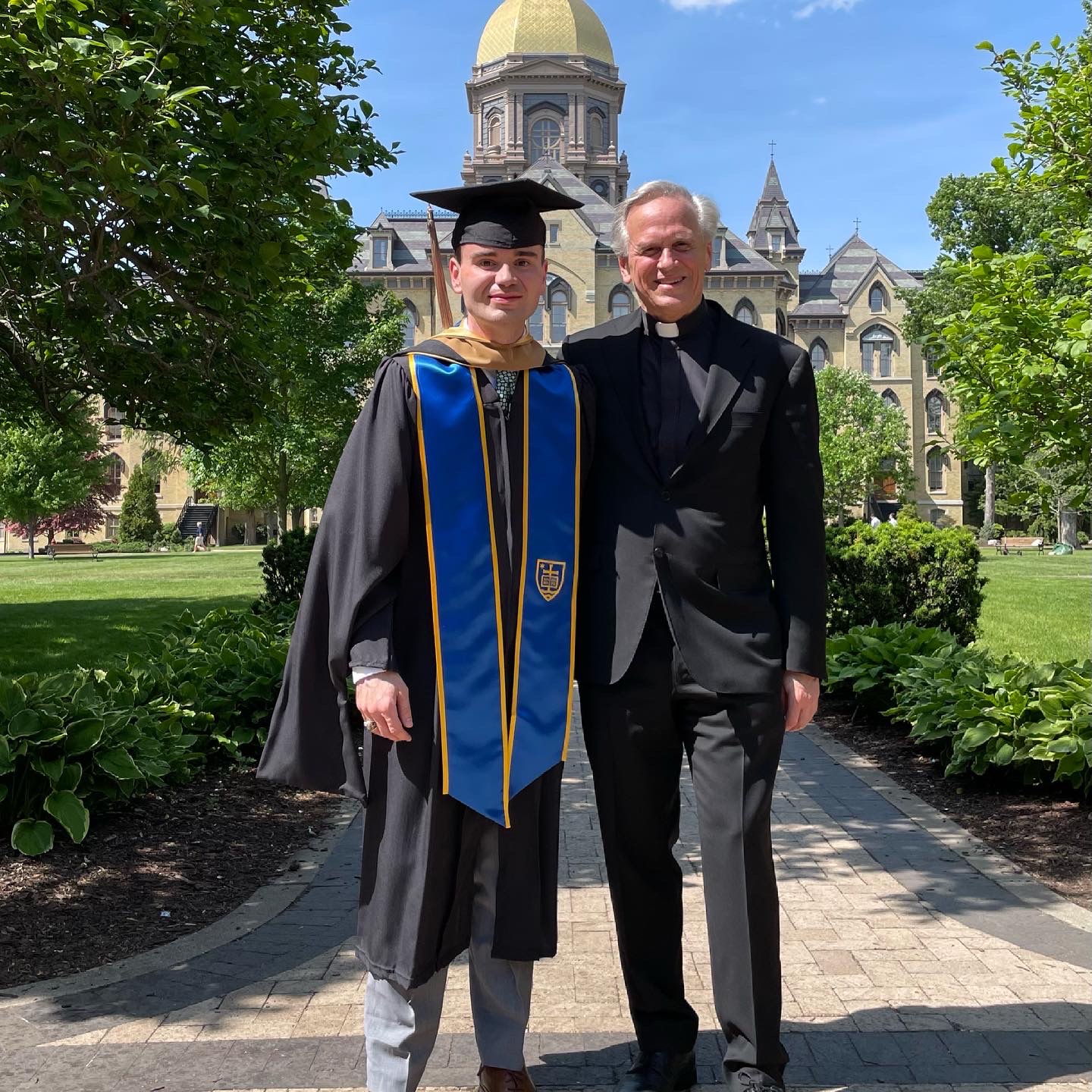 Nathan Stroup poses with The University of Notre Dame's former president Rev. John I. Jenkins, C.S.C. The Golden Dome is in the background. 