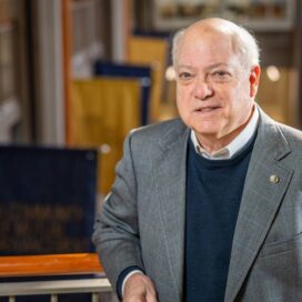 Jim O'Rourke standing against the railing overlooking the Mendoza College of Business atrium with College flags hanging down behind him.