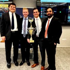 Group of men in suits stand together holding a large trophy.