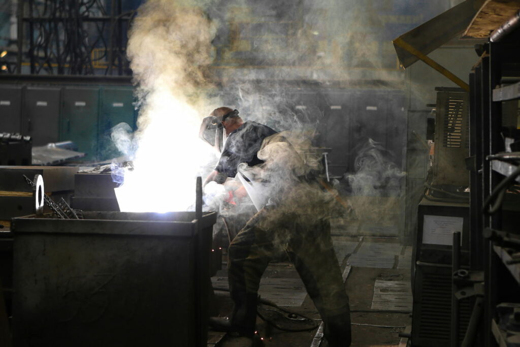 A photo of a man in safety gear welding products in a factory.