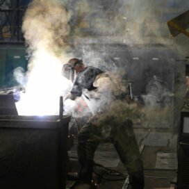 A photo of a man in safety gear welding products in a factory.
