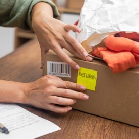 close up of a box with a red garment on it, and a person attaching a note on it that says return.