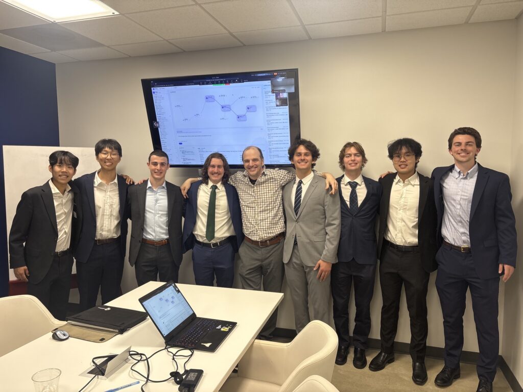 A group of people in business attire in a conference room setting. They are posing as a group.
