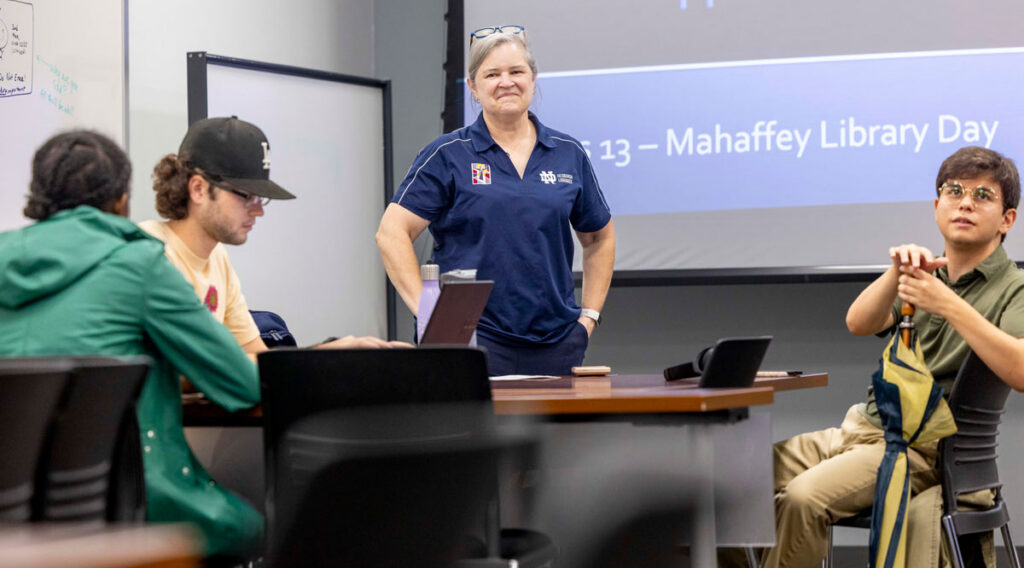 A smiling woman stands in front of students in the library classroom.